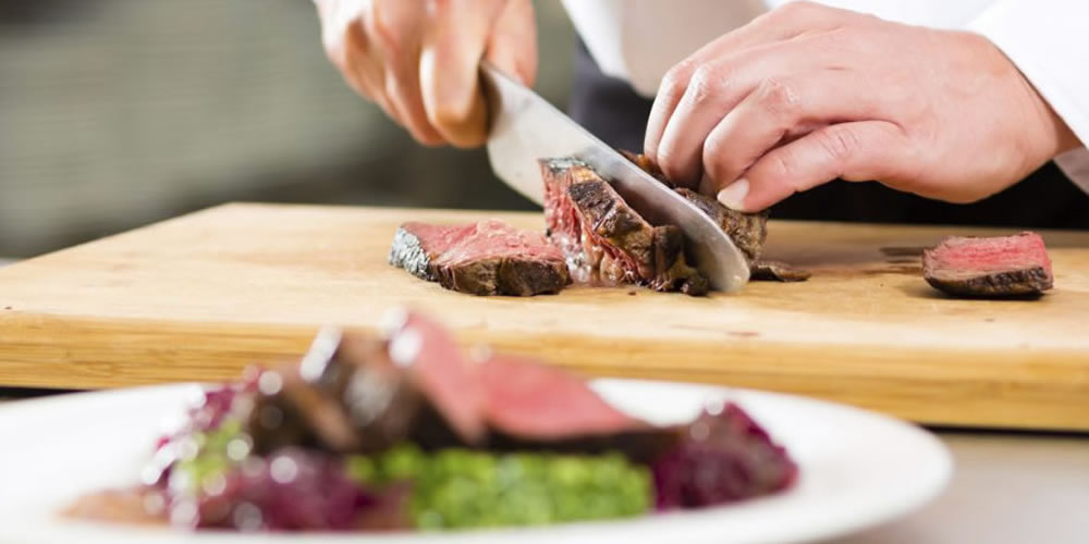 Koch schneidet Fleisch mit einem scharfen Messer